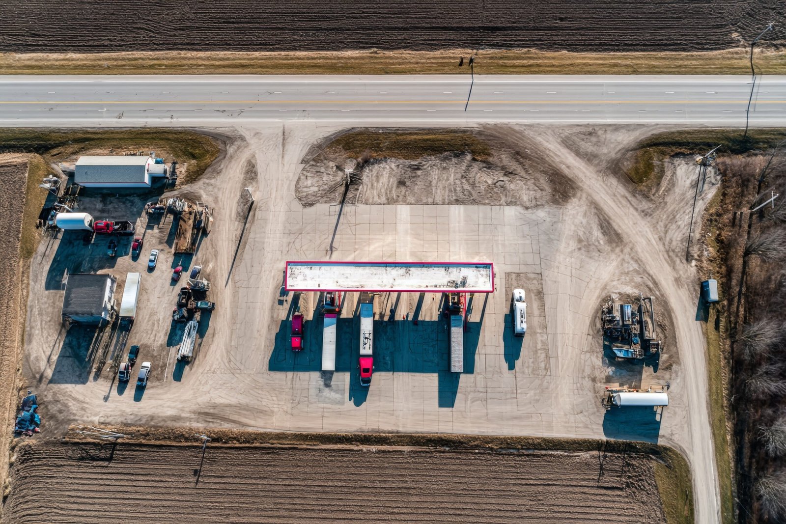 An overhead drone view captures a busy truck stop and gas station adjacent to a highway.